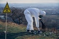 Researcher in protective suit collecting plastic garbage into black waste bag outdoors on a sunny day