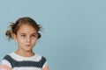 Resentful tight-lipped little girl in striped sweater, hair in buns over blue Royalty Free Stock Photo