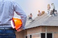 Resident engineer holding yellow safety helmet at new home building under construction site with workers installing concrete tile