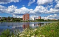 Residential building behind the river, reflected in water, blue sky, white clouds