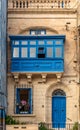 Facade with blue door, window shutters and traditional Maltese wooden balcony in Sliema, Malta.