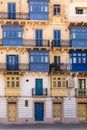 Residential house facade with blue door, window shutters and traditional Maltese wooden balcony