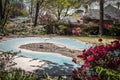 Residential swimming pool in spring before its been opened with tarp and dead leaves in yard with blooming azeleas and landscaping