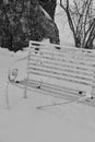Black and white photo of empty park bench in a snowdrift.