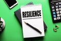 RESILIENCE written in a notebook near the calculator and telephone on a green background