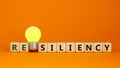 Resiliency symbol. Wooden cubes with word `resiliency`. Yellow light bulb. Beautiful orange background. Business and resiliency