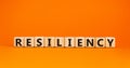 Resiliency symbol. Word `Resiliency` written on wooden blocks. Copy space. Beautiful orange table, orange background. Business a