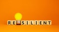 Resilient symbol. Wooden cubes with word `resilient`. Yellow light bulb. Beautiful orange background. Business and resilient Royalty Free Stock Photo