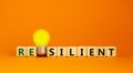Resilient symbol. Wooden cubes with word `resilient`. Yellow light bulb. Beautiful orange background. Business and resilient Royalty Free Stock Photo