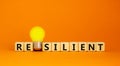 Resilient symbol. Wooden cubes with word `resilient`. Yellow light bulb. Beautiful orange background. Business and resilient