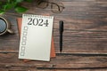 2024 resolutions list in a spiral notebook on wooden table with pen and coffee cup. Creative flat lay Royalty Free Stock Photo