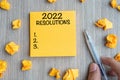 2022 RESOLUTIONS word on yellow note with Businessman holding pen and crumbled paper on wooden table background. New Year start, Royalty Free Stock Photo