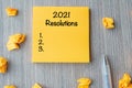 2021 RESOLUTIONS word on yellow note with pen and crumbled paper on wooden table background. New start, Strategy and Goal concept