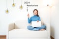 2024 resolutions with young woman pointing resolutions cheerful and happy new year with laptop on the sofa in living room.
