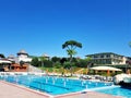 Scene with swimming pools, lounge chaires, pine and palm trees and hotel building Royalty Free Stock Photo