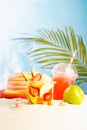 Resort lifestyle - picnic with cold cocktail, fresh tropical fruit salad, sun hat on white sand with palm, sun glare in blue sea. Royalty Free Stock Photo