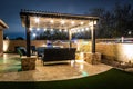 A resort style backyard at night with a waterfall, pergola, and a firepit