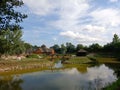 Resort view with houses, meadow, and trees around, a lake reflecting cloudy sky background