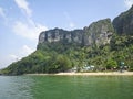 The resort village on the beach under the mountain with rocky steep cliffs, palm trees, yellow sand, azure sea. Royalty Free Stock Photo