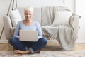 Resourceful mature woman sitting on floor and using laptop Royalty Free Stock Photo