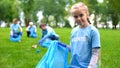 Responsible child volunteer collecting trash in garbage bag smiling on camera