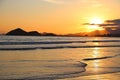 Sunset at the beach. In the background silhouettes of mountains, reddish sky. Beach with reflections in the sand.