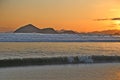 Sunset at the beach. In the background silhouettes of mountains, reddish sky. Beach with reflections in the sand.