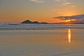 Sunset at the beach. In the background silhouettes of mountains, reddish sky. Beach with reflections in the sand.