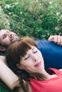 Couple makes a selfie while lying on the grass in flowers. Rest, lovers on a flower meadow. Bearded man and a girl in a red dress Royalty Free Stock Photo