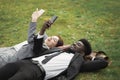 Multiracial well-dressed young business people resting lying on green grass with smartphone Royalty Free Stock Photo