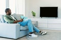 Rest and relax. Black man sitting on the sofa in living room, watching television show, looking at blank plasma tv Royalty Free Stock Photo