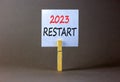 2023 Restart symbol. White paper with words 2023 Restart, clip on wooden clothespin. Beautiful grey table grey background.
