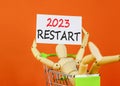 2023 Restart symbol. White paper with words 2023 Restart, human model in shopcart. Beautiful orange table orange background.
