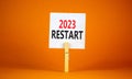 2023 Restart symbol. White paper with words 2023 Restart, clip on wooden clothespin. Beautiful orange table orange background.