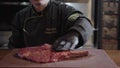 Restaurant chef in black gloves and uniform prepare raw meat on bone, man slather with oily liquid big piece of meat.