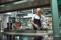 Restaurant chef. Concentrated young chef in black apron is cooking at his modern restaurant kitchen.