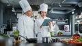 Restaurant Kitchen: Team of Asian and Black Female Chefs use Tablet Computer while Cooking Delicious Royalty Free Stock Photo