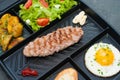 Restaurant lunch, content for the site. Breakfast, cutlet or steak, tomato salad, fried potatoes, croutons and fried egg on black Royalty Free Stock Photo