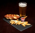 Pretzel hotdog with French fries on a plate made of slate