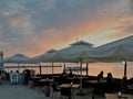Restaurant by the sea with sunset, people at dinner, tables under white umbrellas