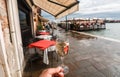 Restaurant terrace and wineglass in a hand on Venice embankment. Bar visitor walking past old cafe and and water canals