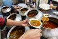 A restaurant worker spooning a mutton curry from the big pot