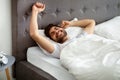 Rested arab man waking up and stretching hands, wellslept guy lying in bed, awakening in cozy bedroom and smiling