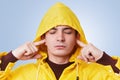 Restful attractive male closes eyes and plugs ears, tries to concentrate and not hear loud noise, wears yellow hood on head, isola Royalty Free Stock Photo