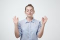 Restful peaceful female feels relaxed in blue shirt, stands near gray wall, tries to concentrate or to be focused