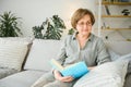 Restful reading. Portrait of thoughtful aged woman reading favorite literature at cozy home. She is lying on pillows on Royalty Free Stock Photo