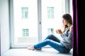 Resting and thinking woman. Calm girl with cup of tea or coffee sitting and drinking on the window-sill at home. Royalty Free Stock Photo