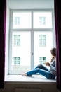 Resting and thinking woman. Calm girl with cup of tea or coffee sitting and drinking on the window-sill at home. Royalty Free Stock Photo