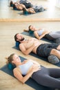 Restorative yoga with a bolster. Group of young sporty attractive people in yoga studio, lying on bolster cushion