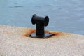 Restored and freshly and painted black old iron mooring bollard screwed on local concrete pier with four metal bolts surrounded